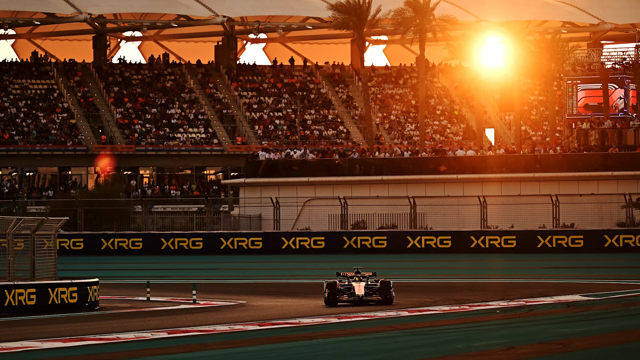 Formula 1 car passing full Yas Marina grandstands at sunset