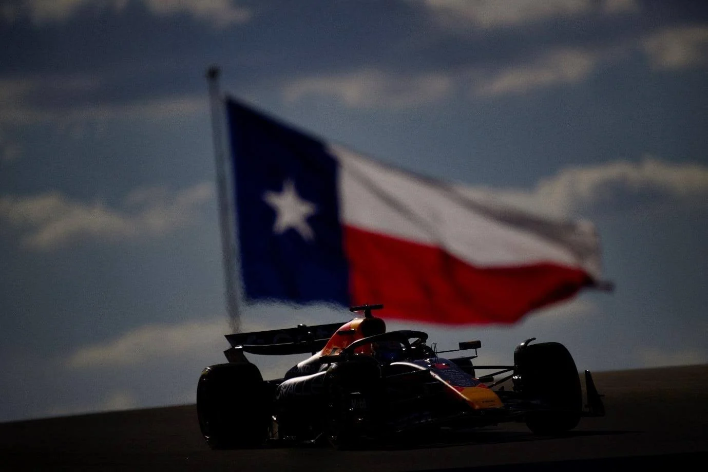Formula 1 car racing at Circuit of the Americas beneath a Texas flag