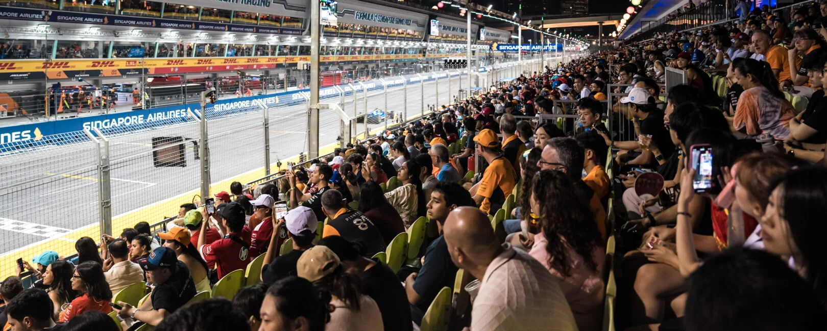 Spectators in the Singapore Grand Prix Pit Grandstand facing the illuminated garages and pit lane